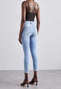 Jeans skinny de color azul claro con cintura alta, que cuentan con bolsillos traseros y detalles de costura. Combinados con sandalias negras de tacón.