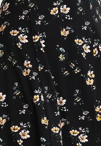 Robe en tissu noir ornée d'un motif floral avec des fleurs blanches et jaunes, texture lisse et coupe ajustée.