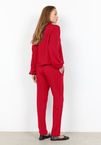 Red matching set featuring a loose long-sleeve top and straight-leg pants, both made from soft fabric. Black flat shoes complete the look.