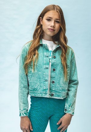 Lichtblauwe denimjas met knoopsluiting en klepzakken, gecombineerd met teal geklede leggings met een patroon. Glad textuur, cropped ontwerp.