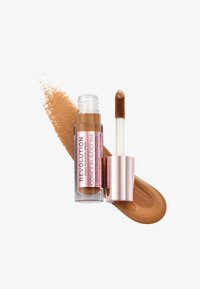 Correcteur liquide dans un tube transparent avec un capuchon en or rose, doté d'un applicateur en forme de pied de faon. Accompagné d'un échantillon lisse de couleur caramel.
