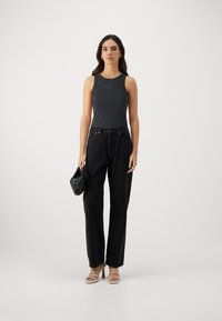 Svart ribbet tanktop med subtil logo, parret med højtaljede løse sorte jeans og stroppede beige hæle. Accessories inkluderer en lille sort taske.