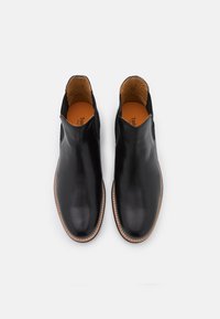 Bottes chevillardes en cuir noir à texture lisse, côtés élastiques et semelle marron assortie. L'intérieur présente une semelle intérieure orange.