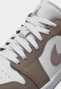 Pantof sport înalți albi și taupe, cu șireturi albe, suprapuneri din piele întoarsă și un logo swoosh semnătură pe lateral.