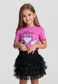 T-shirt grafico rosa con design di pozioni abbinato a una gonna in tulle nera a strati, che mette in mostra una texture arricciata e una vita aderente.