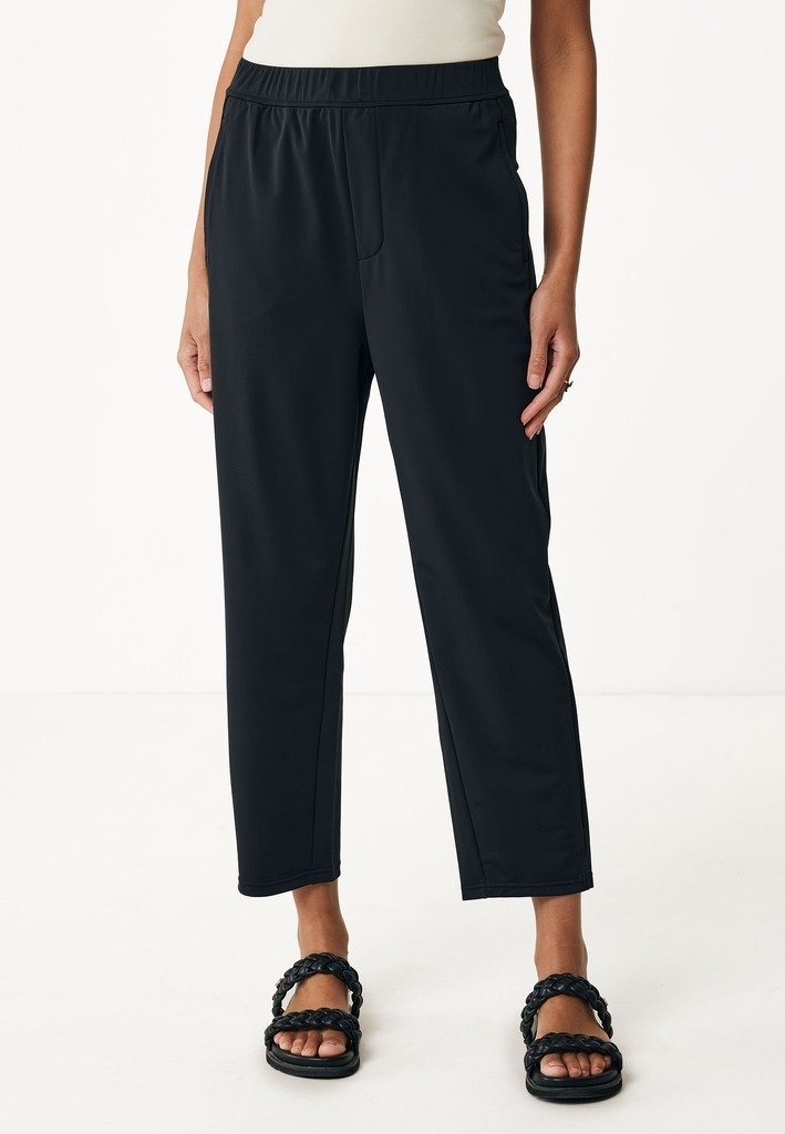 Svarta, löst sittande, cropped byxor med elastiskt midjeband och sidfickor, tillverkade av ett smidigt, lätt tyg, tillsammans med svarta sandaler.