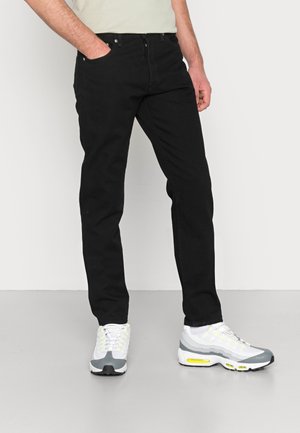 Jeans de mezclilla negra con corte recto, diseño de cinco bolsillos y detalles metálicos, combinados con zapatillas deportivas grises y blancas.