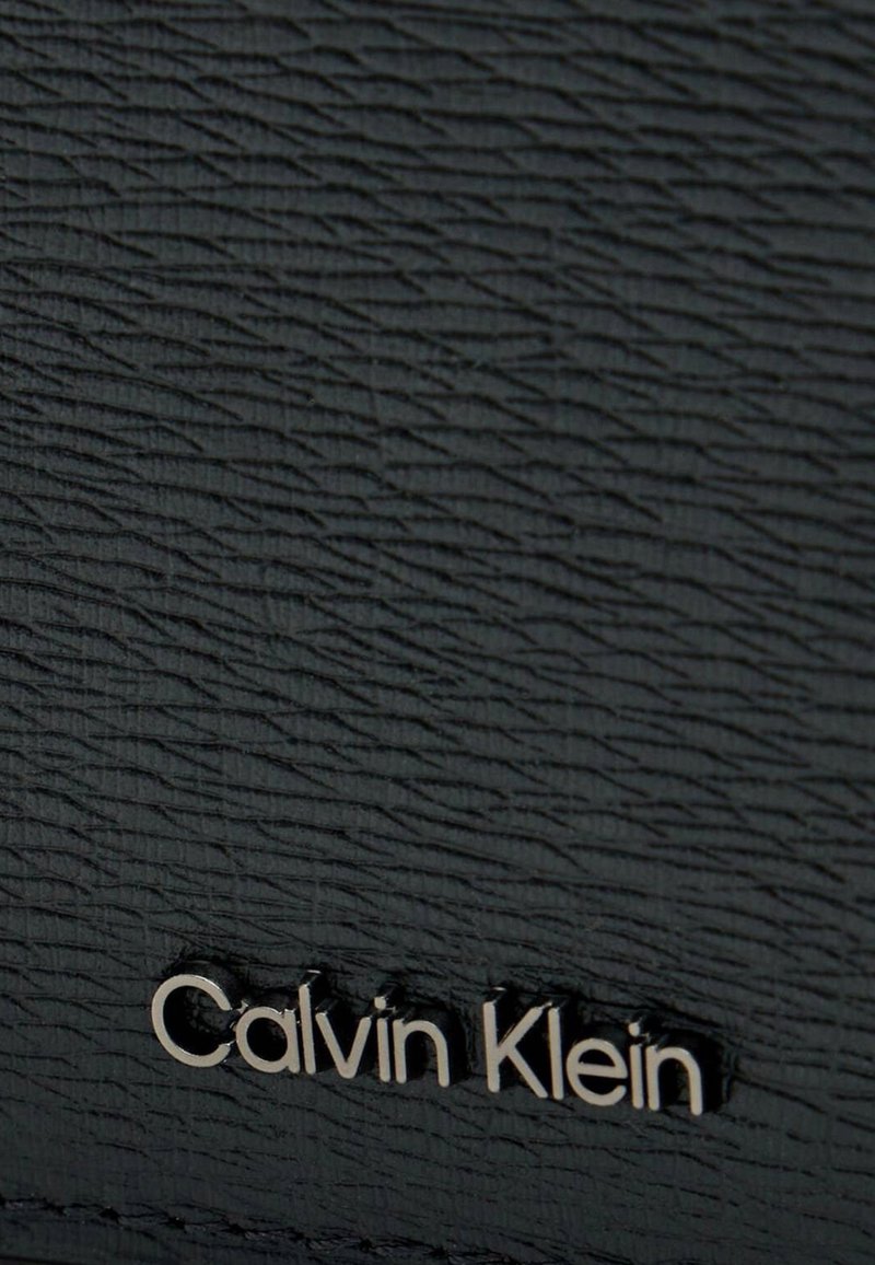 Pelle nera testurizzata con motivo in rilievo e logo "Calvin Klein" metallico argentato in basso.