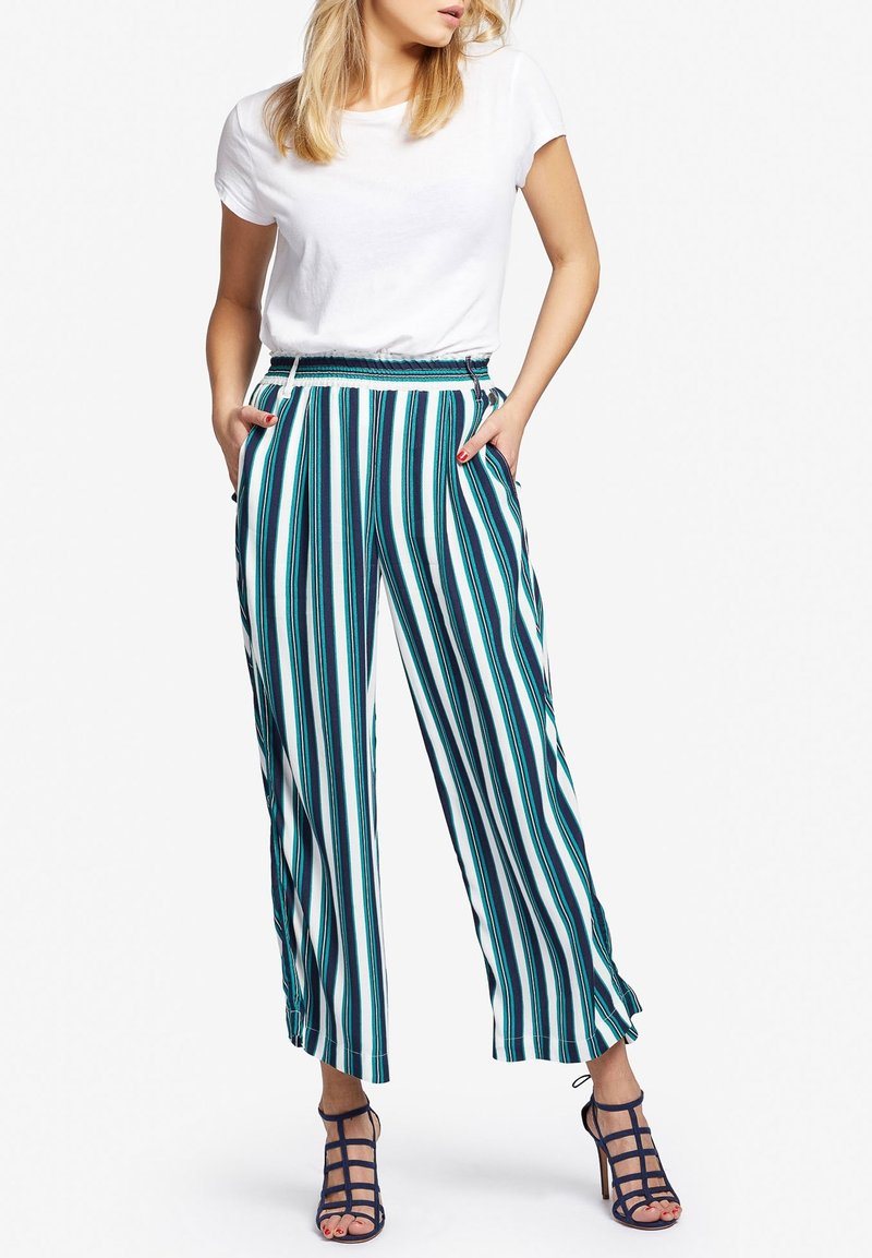 Witte, getailleerde T-shirt gecombineerd met wijde, verticaal gestreepte broek in teal, marineblauw en wit. De broek heeft zakken en een elastische tailleband.