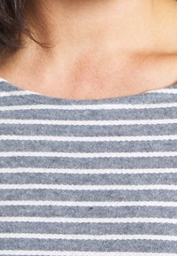 Niebieska i biała bluzka w paski wykonana z miękkiej bawełny. Posiada okrągły dekolt i widoczną teksturę, z wąskimi białymi paskami na ciemniejszym tle.