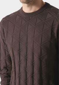 Brauner Strickpullover mit einem strukturierten Rautenmuster, rundem Halsausschnitt und langen Ärmeln. Der Stoff erscheint weich mit einem subtilen Glanz.