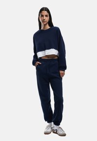 Marineblå cropped sweatshirt med et hvidt lag under, parret med løstsiddende marineblå joggers. Begge dele har en blød tekstur og et afslappet design.