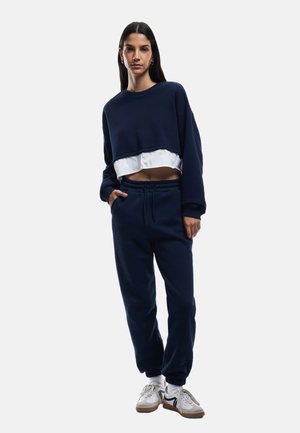 Marineblå cropped sweatshirt med et hvidt lag under, parret med løstsiddende marineblå joggers. Begge dele har en blød tekstur og et afslappet design.