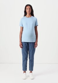 Tricou scurt cu mânecă, de culoare albastră cerului, cu guler rotund, asortat cu blugi deschiși, tapered, și adidași albi.