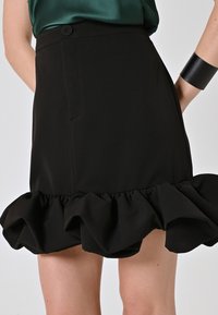 Gonna nera con orlo a balze svasato, vita piatta con chiusura a bottone e texture di tessuto liscia.