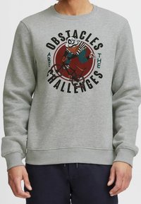 Szary sweatshirt z grafiką pandy na rowerze, z wyboldowanym napisem "Przeszkody są wyzwaniem". Miękka tekstura, okrągły dekolt.