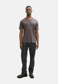 Tricou gri cu guler în V, confecționat din bumbac, asortat cu jeansi negri. Modelul poartă pantofi negri, afișând un look casual.