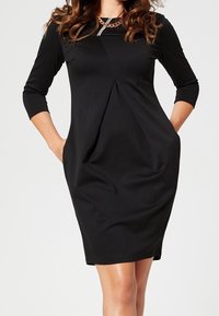 Robe noire à manches trois-quarts, décolleté arrondi, détail de plis à l'avant, deux poches latérales, texture lisse et silhouette ajustée.