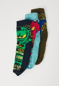 Drei farbenfrohe gemusterte Socken mit Zeichentrick-Ninja-Gesichtern in grünen, roten und blauen Farbtönen auf einem weißen Hintergrund gestapelt.