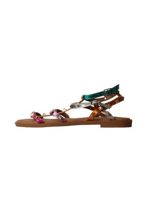 Sandale plate avec des brides métalliques multicolores et une boucle à la cheville sur une semelle marron, vue de côté sur fond blanc.