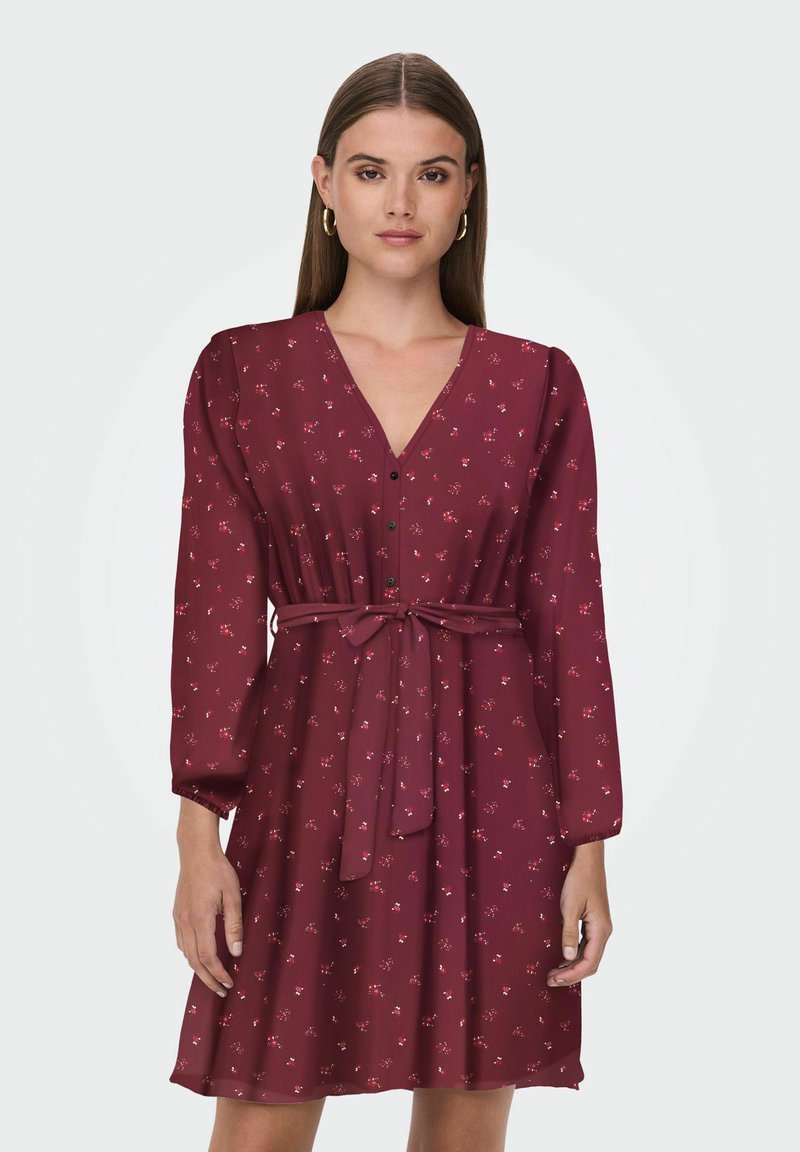 Robe bordeaux avec un décolleté en V, des manches longues, une taille à nouer et de petits motifs floraux ; fabriquée à partir d'un tissu léger et respirant.