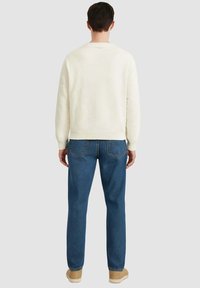 Maglione crema con tessuto strutturato, polsini e orlo a coste, abbinato a jeans blu e scarpe beige, visto da dietro.