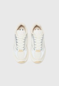 White and beige sneakers with mesh and leather materials, featuring reflective silver accents, white laces, and textured soles.