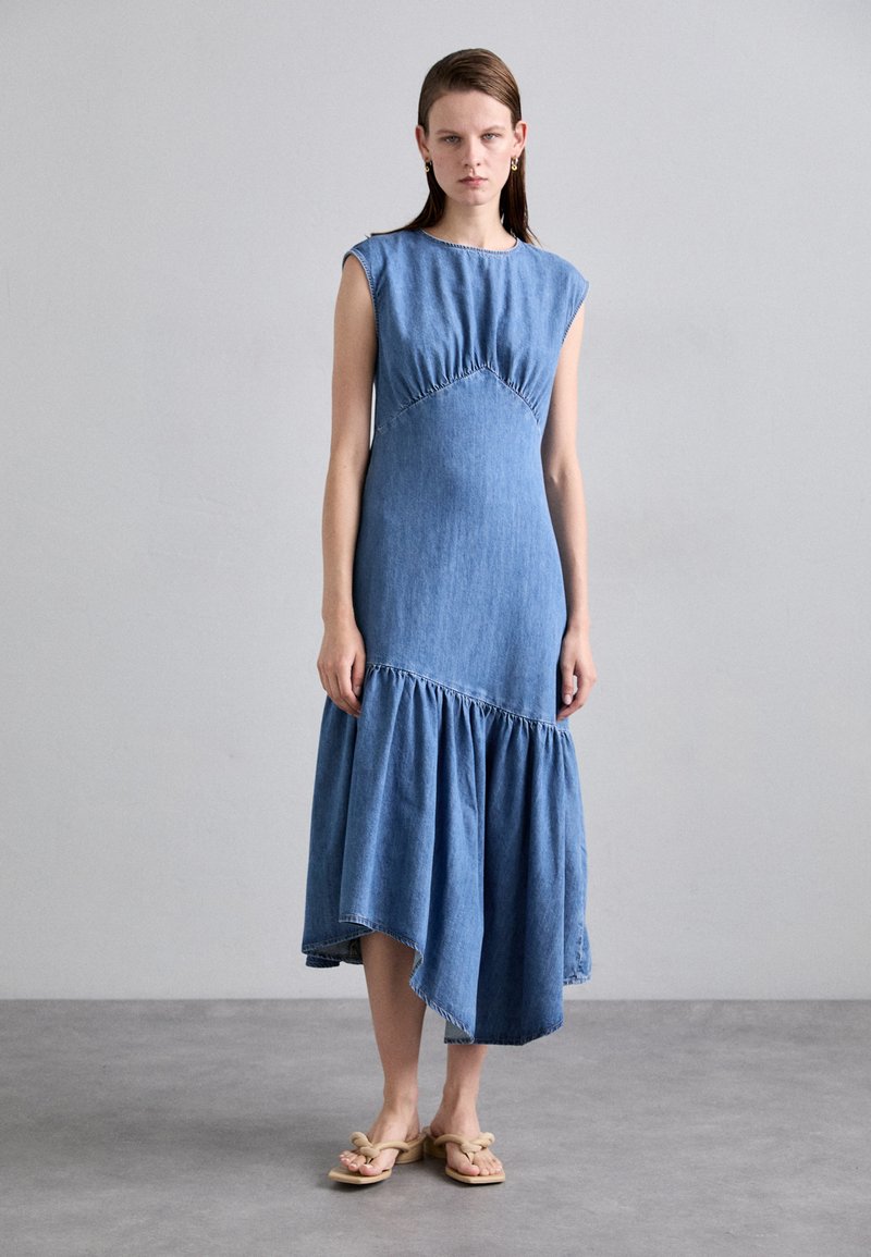 Denim jurk met korte mouwen, geplooide lijfje, en asymmetrische uitlopende zoom. Lichtblauwe kleur; gladde textuur met stikseldetails.