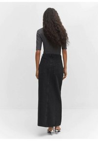 Gonna maxi in denim nero con vita aderente, due tasche posteriori e leggero svaso verso l'orlo. Abbinata a un top grigio aderente.