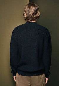Mørkeblå, chunky striktrøje med ribbet struktur og rund halsudskæring. Løs pasform og lange ærmer. Har samlede manchetter og kant.