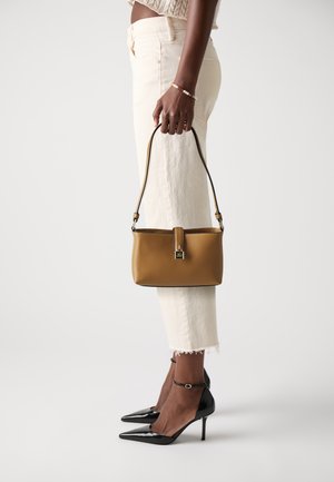 Brown leather handbag with a short strap, featuring a rectangular shape and a gold-tone clasp. Paired with light-colored, cropped pants and black heels.
