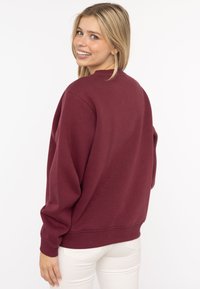 Burgunderfarbener Rundhalsausschnitt-Sweatshirt aus weichem Stoff, mit lockerer Passform, gerippten Bündchen und Saum. Minimalistisches Design ohne sichtbare Logos.
