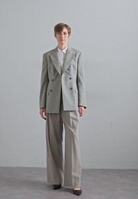 Oversized gray plaid blazer with peaked lapels, double-breasted buttons, and wide-leg gray trousers. Black pointed-toe heels.