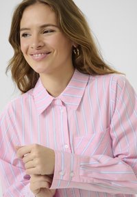Camicia a righe rosa, con righe verticali blu e bianche, colletto a punta e taschino sul petto. Polsini abbottonati e tessuto morbido.