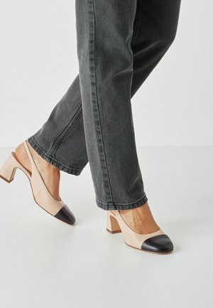 Beige Slingback-Pumps mit schwarzer Kappe, quadratischem Blockabsatz und glattem Leder, kombiniert mit dunkelgrauer Denim-Hose.