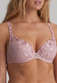 Pink embroidered bra featuring floral patterns, dotted sheer overlay, adjustable straps, and a subtle decorative accent at the center.