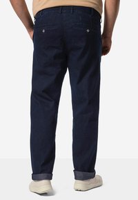 Jeans de mezclilla azul oscuro con un diseño de pierna recta, que cuentan con bolsillos traseros con botones de metal y puños enrollados, combinados con zapatillas de color claro.