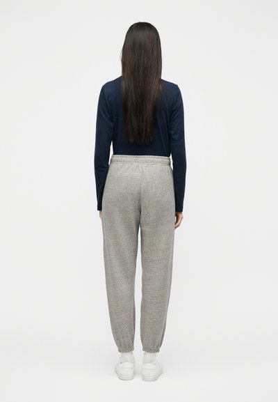 Άτομο με μακριά σκούρα μαλλιά που φοράει μπλε μπλούζα με μακριά μανίκια, γκρι φόρμα, λευκές κάλτσες και λευκά αθλητικά παπούτσια, από πίσω όψη.