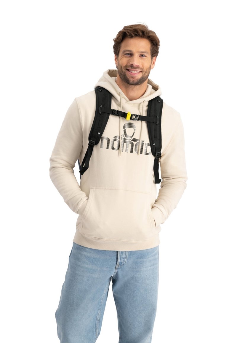Beige Kapuzenpullover mit einem grafischen "Nomade"-Logo, Kängurutasche und Kapuze mit Zugkordel. Getragen über blauen Jeans und ergänzt durch einen schwarzen Rucksack.