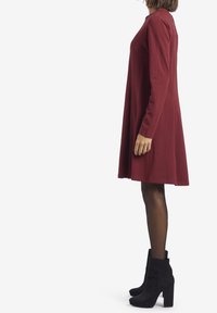 Abito lungo a maniche, color maroon, con busto aderente e gonna svasata, abbinato a stivaletti neri in suede con tacco a blocco.