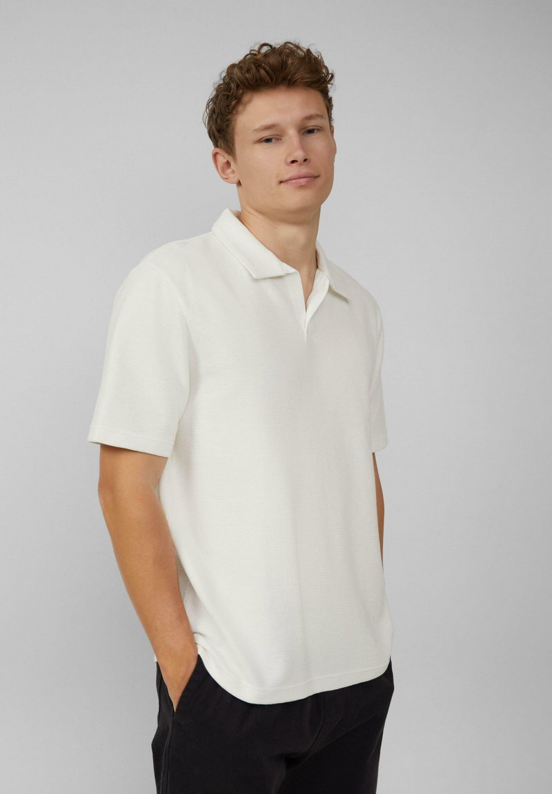 Witte polo met korte mouwen van een gestructureerde brei, met een klassieke kraag en rechte zoom, gecombineerd met donkere broeken.