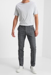 Grijze katoenen t-shirt en geruite grijze broek. De broek heeft een slim fit met een subtiel patroon. Witte sneakers maken de outfit compleet.