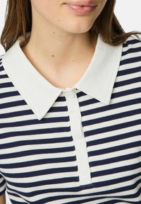 Jūras spēku un baltu svītrainu polo krekls ar baltu apkakli, divu pogu aizdari un ribota tekstūra ap kaklu.