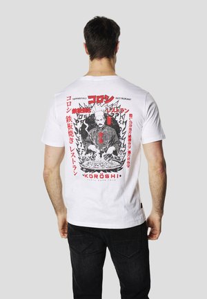 Camiseta de algodón blanca con un gran estampado gráfico en la parte trasera. El diseño incluye un chef, llamas y texto en rojo y negro.