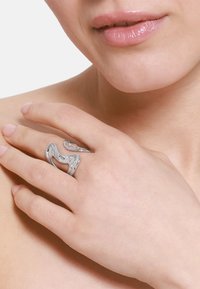 Sølvmetallring med et bølgete, organisk design. Vist på en hånd, som viser sin polerte overflate og unike form.