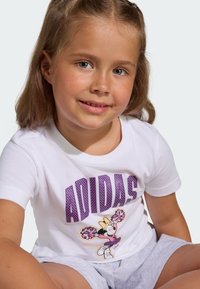 Biele tričko s krátkym rukávom s fialovým logom "ADIDAS" a grafikou postavy s pom-pommi. Sivé šortky s mäkkou textúrou.