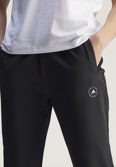 Schwarze Sporthosen mit einer glatten, leichten Textur. Mit einem weißen runden Logo am linken Oberschenkel und seitlichen Taschen.