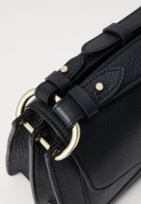 Black textured leather handbag featuring a structured shape, gold-tone hardware, and adjustable straps with buckle details.