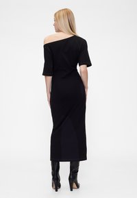 Fekete váll nélküli ruha rövid ujjakkal, testhezálló szabású és bokáig érő kialakítással, térdig érő fekete sarokcsizmával párosítva.