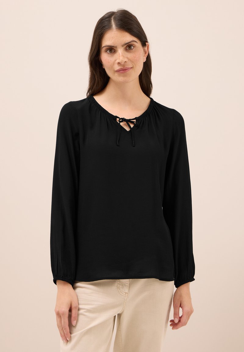 Blusa nera a maniche lunghe con scollatura rotonda, dotata di dettagli arricciati e un laccio sul davanti. Tessuto morbido con una vestibilità comoda.